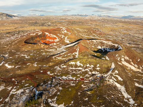 Aerial view of the volcanic craters of Grabrok with reddish soil, patches of snow, and mossy terrain in the vast landscape of Iceland.