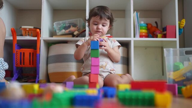 baby plays with toy blocks on floor. development of fine motor skills in children concept. baby daughter girl builds a tower from toy lifestyle cubes indoors kindergarten