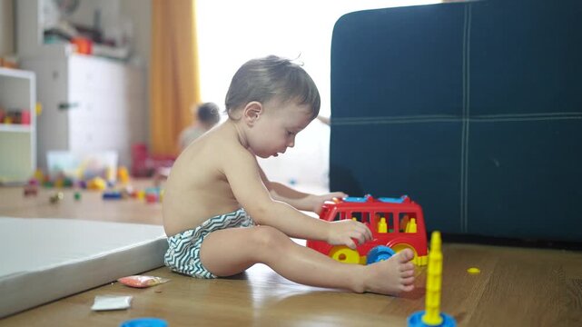 baby child playing toy car bus on floor in kindergarten. happy family kid concept. baby son playing red bus toy bus indoors. child boy blond plays with lifestyle a toy car in kindergarten