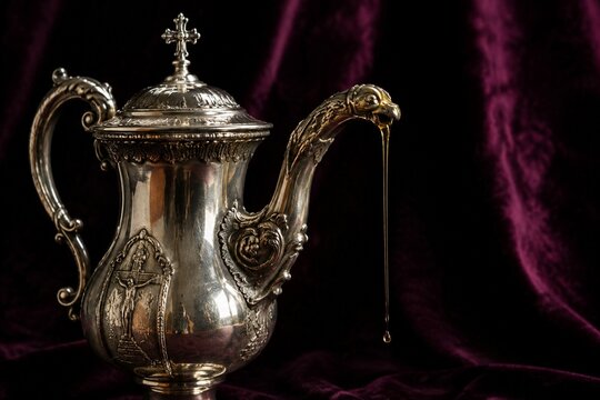 An ornate silver chrismatory with a thin golden stream, on dark velvet with dramatic lighting.
