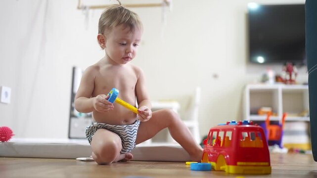 baby child playing toy car bus on floor in kindergarten. happy family kid concept. baby son playing red bus toy bus indoors. child boy lifestyle blond plays with a toy car in kindergarten