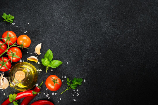 Fresh tomatoes, basil, rosemary, spices and olive oil bottle on black table.