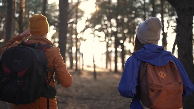 two hiker work as team. with backpacks walking in winter in a forest park in the sunny glare sun at sunset. Two tourists travel hiking in forest park, overcoming difficulties, teamwork concept
