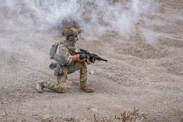 Fototapeta premium Soldier takes cover during training in a smoky area with gravel ground in a military exercise setting