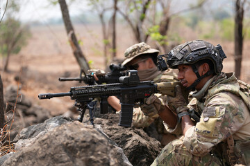 Fototapeta premium Military personnel take position behind rocks during an exercise in a forested area in the daytime