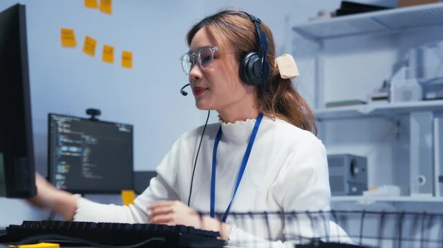 Confident Asian Female Customer Service Agent talking, typing and helping client via headset using computer in call center office. Call Center Representative Assisting a Customer During a Live Support