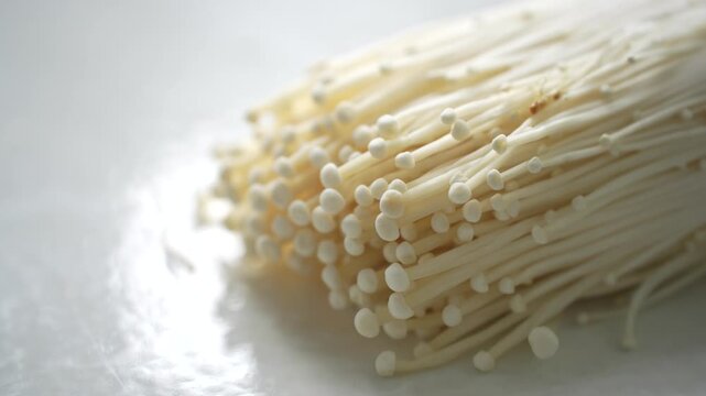 Fresh enoki mushrooms on a white surface, ready for cooking. Suitable for concepts of fresh ingredients, healthy food, home cooking, and organic produce