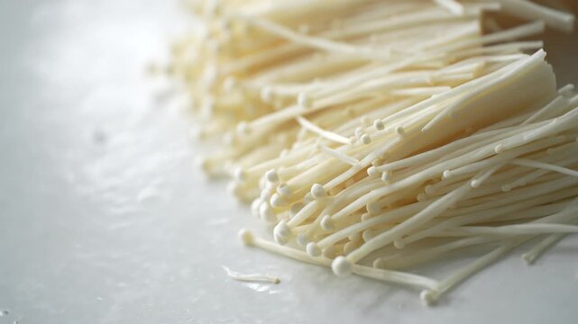 Fresh enoki mushrooms on a white surface, ready for cooking. Suitable for concepts of fresh ingredients, healthy food, home cooking, and organic produce
