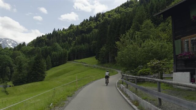 Professional road bike trip adventure showing a male athlete in a helmet climbing a winding asphalt road towards the cloudy peaks of Fellhorn mountain in Oberstdorf area Bavaria Europe