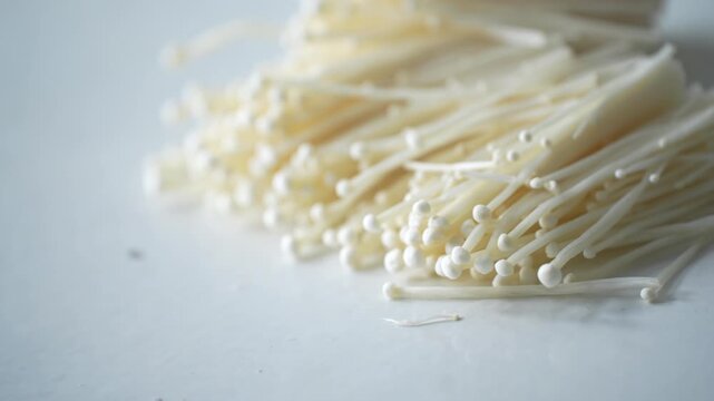Fresh enoki mushrooms on a white surface, ready for cooking. Suitable for concepts of fresh ingredients, healthy food, home cooking, and organic produce