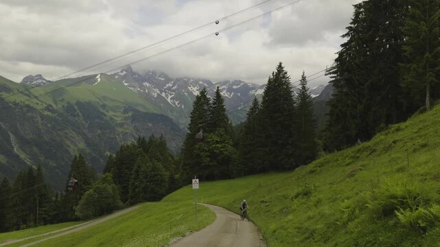 Athletic man riding a gravel bike on a scenic paved mountain road with sharp serpentine curves making a vertical ascent towards Fellhorn summit in Oberstdorf region of wild Bavaria Germany