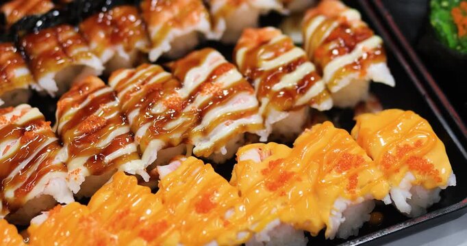 Assorted sushi rolls topped with sauces and roe, beautifully arranged. Ideal for Japanese cuisine, restaurant, buffet, fresh seafood, gourmet food, and dining concepts, close-up