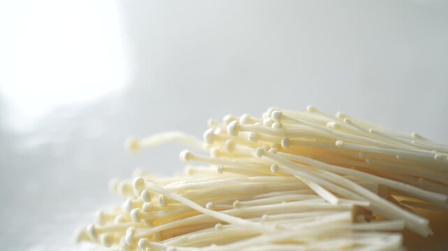 Fresh enoki mushrooms on a white surface, ready for cooking. Suitable for concepts of fresh ingredients, healthy food, home cooking, and organic produce