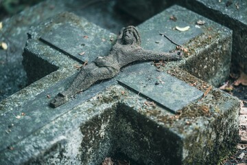 Zabytkowy kamienny krzyż nagrobny z rzeźbą Jezusa Chrystusa pokryty mchem. Detal ze starego cmentarza symbolizujący wiarę i przemijanie. © Henryk Niestrój