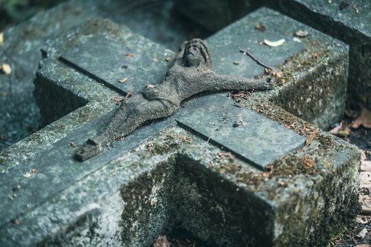 Zabytkowy kamienny krzyż nagrobny z rzeźbą Jezusa Chrystusa pokryty mchem. Detal ze starego cmentarza symbolizujący wiarę i przemijanie.