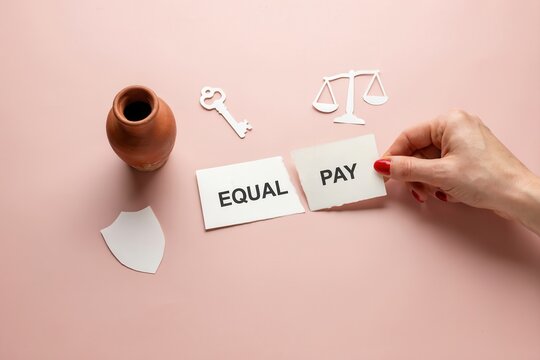 A hand holds equal pay cards with scales and key on a pink background