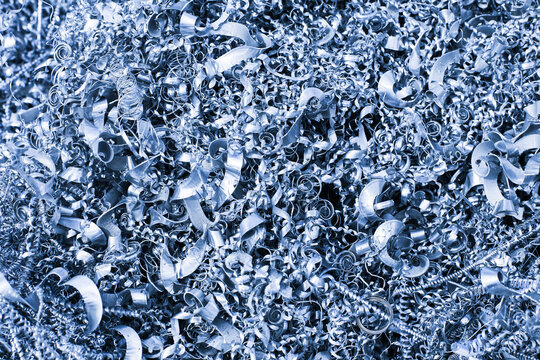 Metal shavings form dense industrial waste. Curled steel chips cover the surface. Machining background shows metalworking debris. CNC production creates scrap. Recycling raw metal remains.