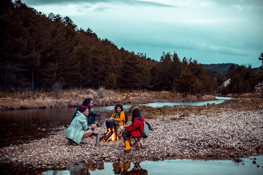 Family camping by a riverside campfire in pine forest