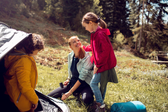 Mother with children setting up tent in forest meadow