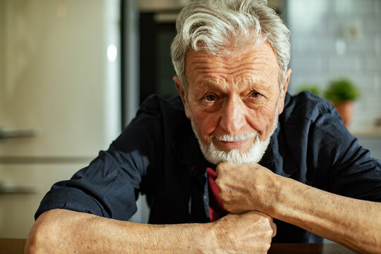 Smiling senior man resting chin on hands in kitchen