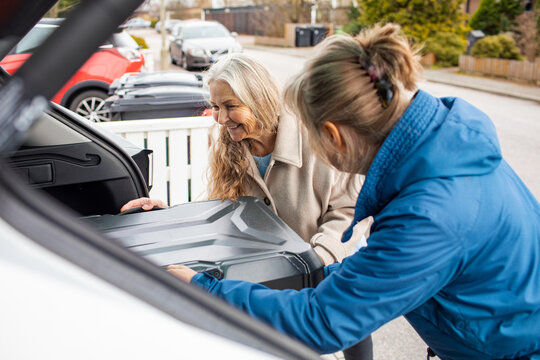 Two women loading suitcase into car trunk on suburban street