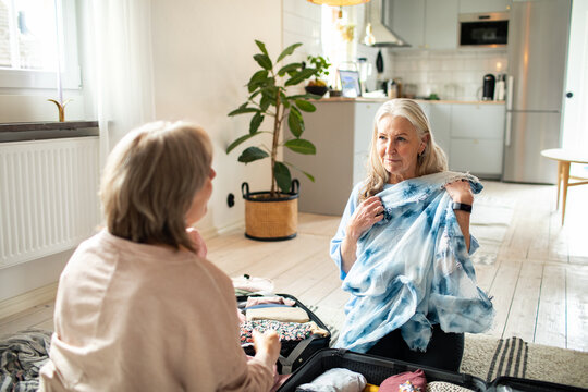 Two senior women packing a suitcase at home