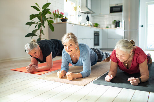 Senior women doing plank exercise together in home kitchen