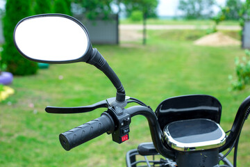 Obraz premium Close-up view of motorcycle handlebar with mirror, throttle grip, and control buttons, set against a blurred green outdoor background
