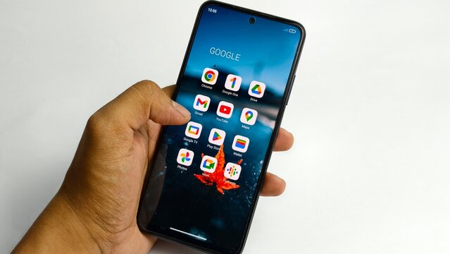Ipoh,Malaysia - 04 July 2026: A person's hand holds a smartphone displaying various Google app icons on its screen against a plain white background.