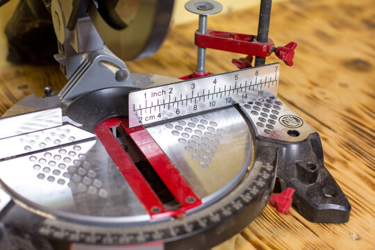 Close-up of a miter saw with a measuring scale and red adjustment knobs on a wooden workbench, showcasing precision cutting tools and equipment