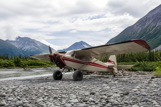 Old Bush Plane Featuring Large Tundra Tires Parked Along Rocky River Gravel Bar Photorealistic Photography