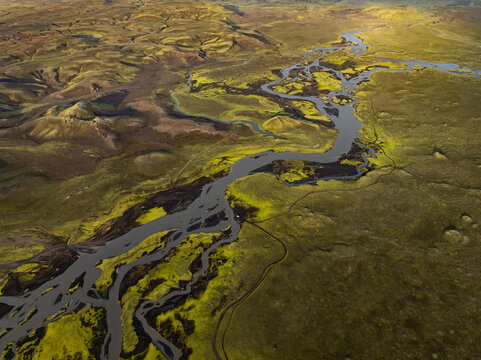 Aerial view of a winding braided river flowing through mossy volcanic terrain in Iceland.