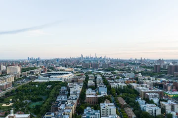 Wide aerial view over New York City skyline with dense residential blocks, stadium, river corridors, distant towers, and soft evening light across broad urban expanse © 21AERIALS