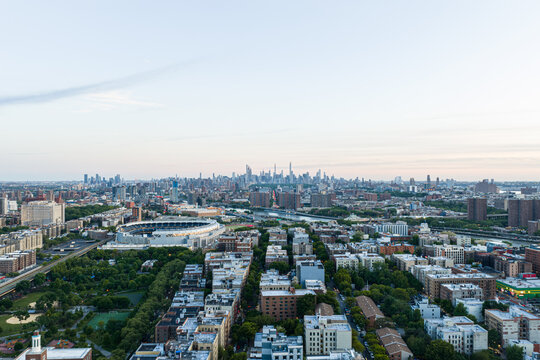 Wide aerial view over New York City skyline with dense residential blocks, stadium, river corridors, distant towers, and soft evening light across broad urban expanse
