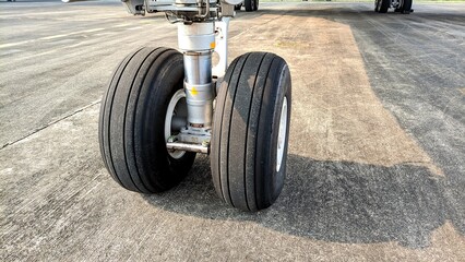 Close-up front view of an aircraft nose landing gear with dual tires parked on the airport apron © Sarmiko.id