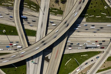 dynamic aerial view of urban freeway interchange with cars and highway overpasses in gray concrete and asphalt setting, showcasing vibrant traffic flow and urban development. © 21AERIALS