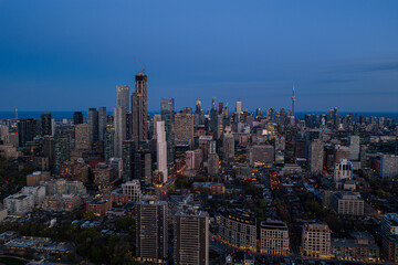 Obraz premium Toronto skyline at dusk with illuminated high-rise towers, construction crane, and wide urban panorama under deep blue evening sky above dense downtown district near lake horizon