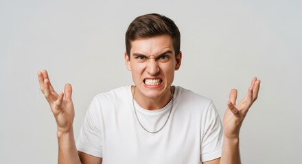 Fototapeta premium Portrait of Furious Young Man Expressing Anger and Frustration with Clenched Teeth and Raised Hands on White Background