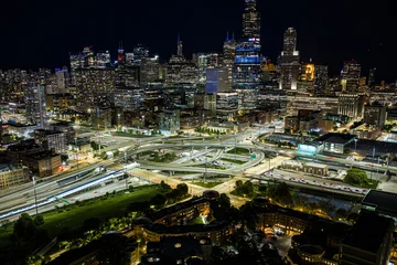 illuminated chicago skyline at night from aerial perspective with dynamic and vibrant urban environment and highway interchanges featuring high-rise buildings, parked cars, concrete and gla. © 21AERIALS