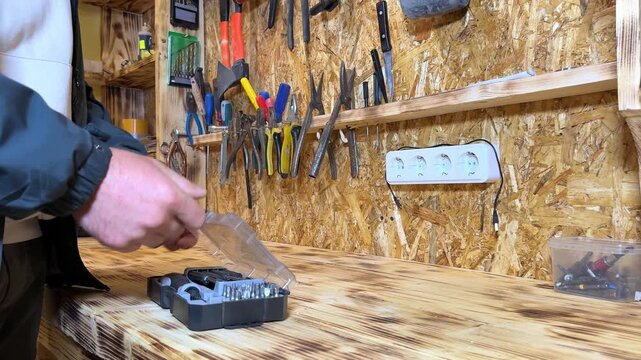 Male technician in gray jacket prepares tools from a toolbox on a wooden workbench surrounded by various hand tools in a well-organized workshop