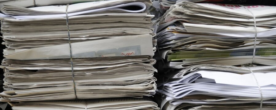 Stacks of newspapers bound with wire, waiting to be recycled. Gray tones suggest age and accumulation. No people, no animals, no plants visible. Ideal for media, sustainability, or urban decay themes