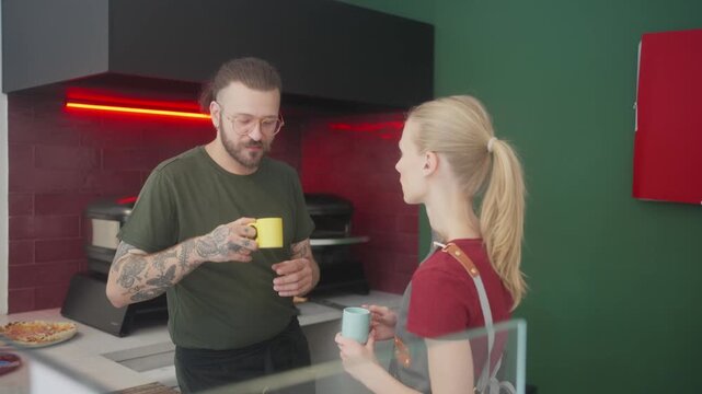 Male and female chef colleagues talking during coffee break in professional kitchen

