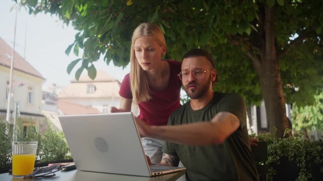 Man and woman freelance professionals working on laptop in outdoor caf&eacute; garden in financial district, smiling business teamwork concept