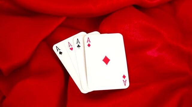 Four aces playing cards arranged in a fan on red silk fabric background poker game gambling casino