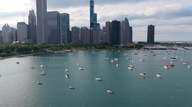 Sailing boats anchored in Monroe Harbor with Chicago's downtown skyline featuring iconic skyscrapers like Vista Tower during an overcast summer day