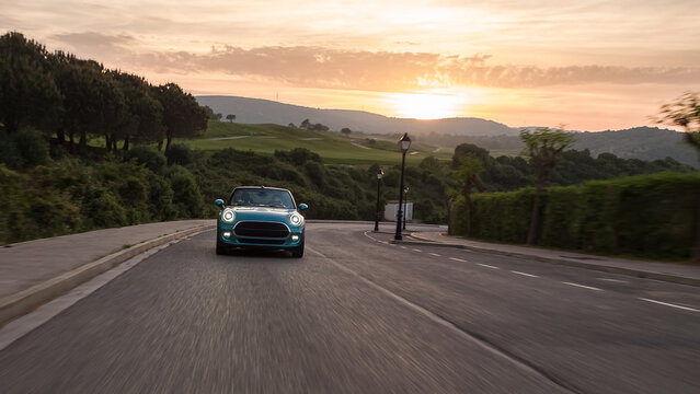 Convertible car driving on winding road at sunset