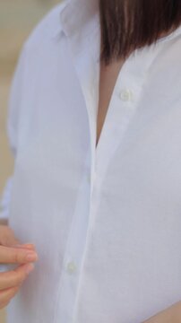 Close-up of a woman adjusting a white shirt and placing her hand in a pocket,