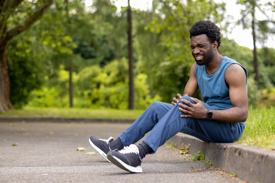 Runner sitting on a curb gripping his knee, feeling intense pain after a sport accident, highlighting themes of health issues, urgency, and injury prevention in athletics