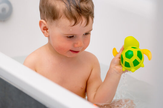 Happy child enjoying water play with a bright turtle toy during bath time.