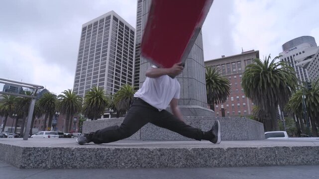 Man Swinging Red Painted Board on Monument Plaza Steps - Low, Steady Cam Angle